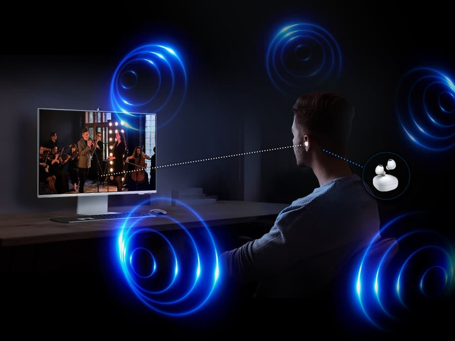 There is a man sitting in front of the monitor. He is listening to the content on the monitor with a Galaxy Buds. Around him, there are some circles which represent spatial sound experience of 360 Audio Mode.